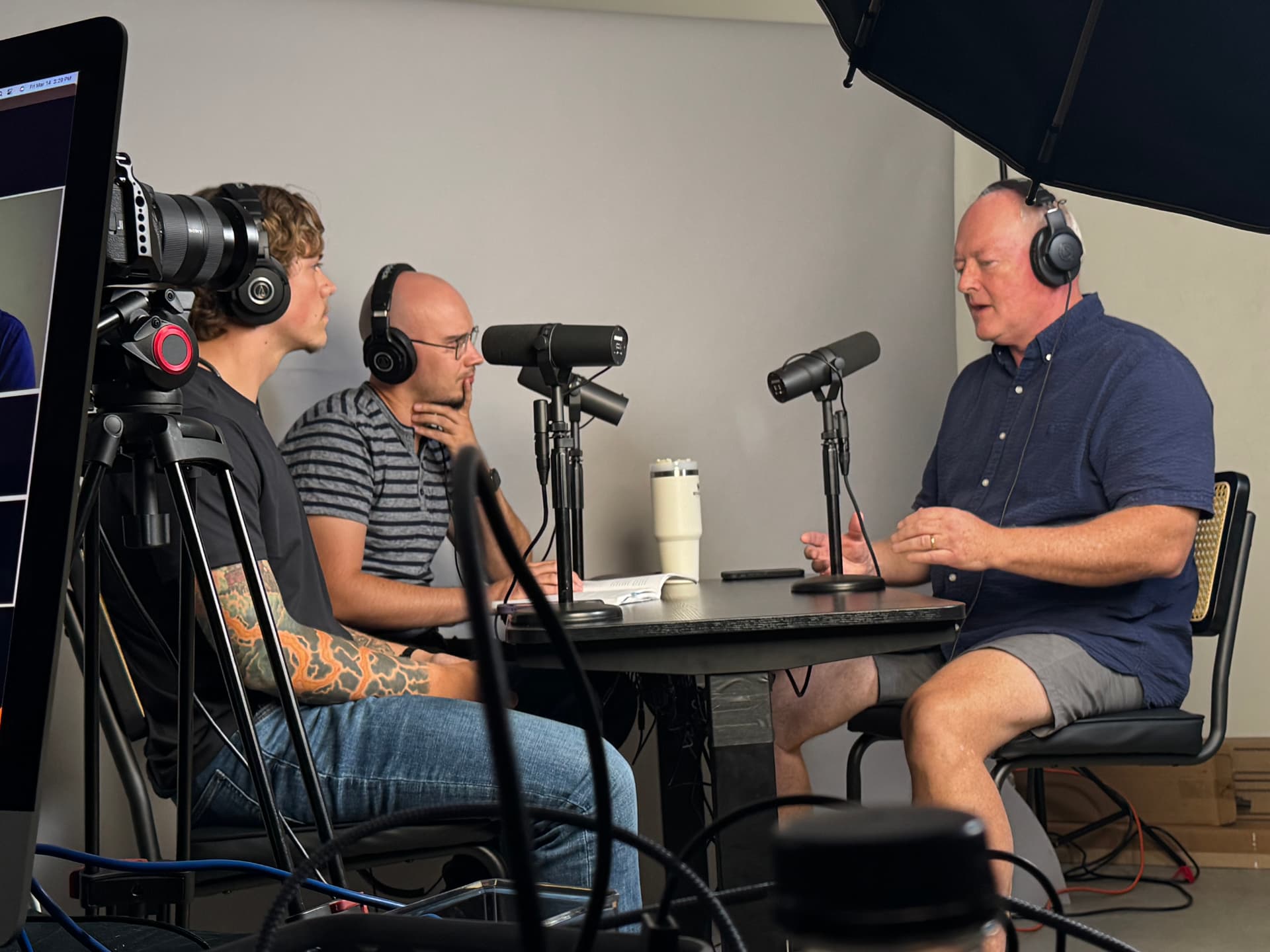 Patrick Talbot being interviewed in a podcast studio, seated at a microphone with two hosts.